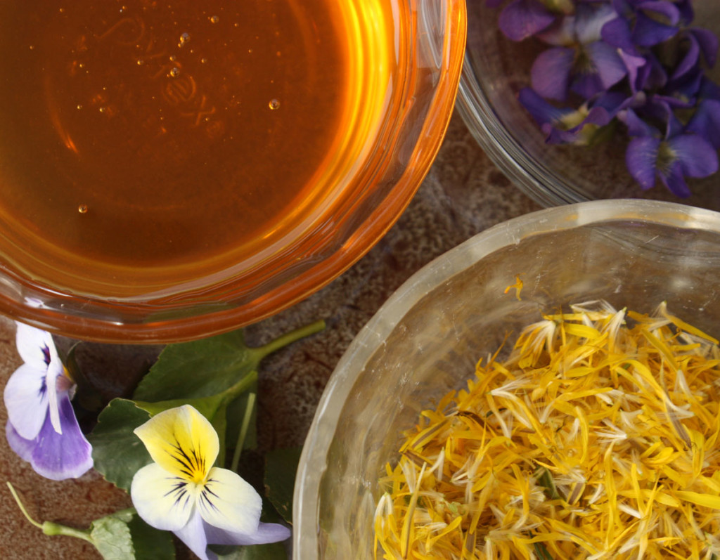 jar of dandelion petals with a jar of honey and a few violet and pansy flowers
