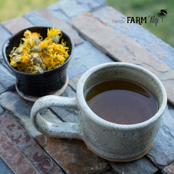 pottery cup filled with calendula tea beside a black pottery bowl filled with dried calendula flowers