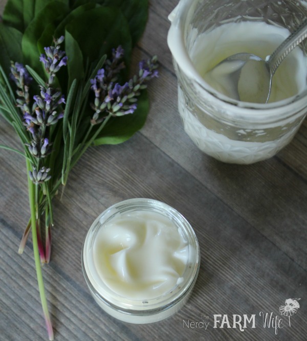 a fresh batch of lavender plantain lotion in a glass jar with fresh lavender and plantain sprigs on a wooden background