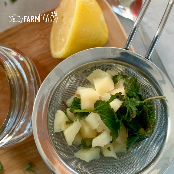 stainless steel strainer with chopped fresh ginger root and lemon balm leaves