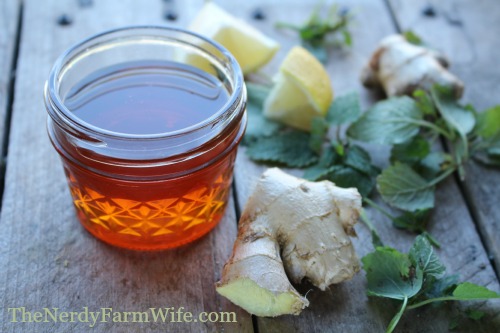 small jar of raw honey and fresh ginger and lemon balm leaves on a wooden background