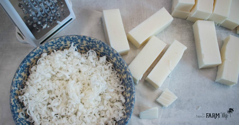 Blue and white bowl filled with grated coconut laundry soap with grater and soap sticks nearby