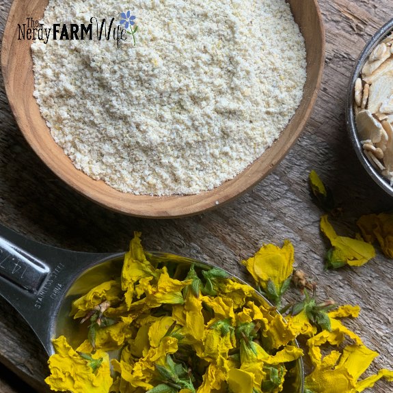 small wooden bowl with floral cleansing grains on a wooden surface beside stainless steel tablespoon filled with dried forsythia flowers