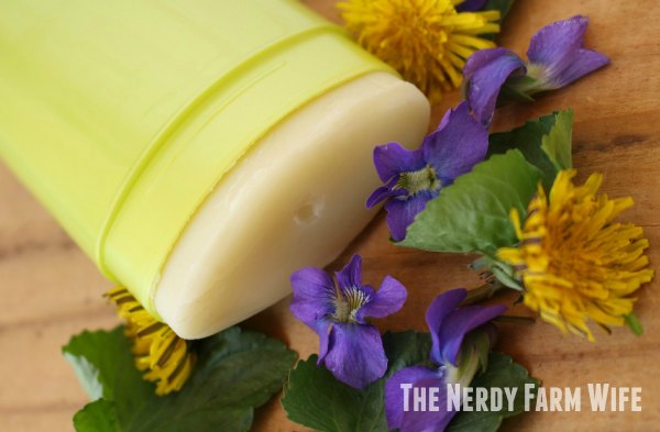 homemade deodorant in a green tube on a wooden background with fresh violets and dandelion flowers
