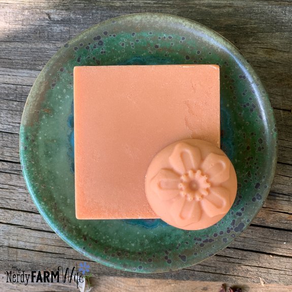 two soaps made with red clay, on a dark green pottery plate and wooden background