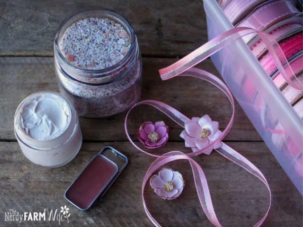 group of skin care products including lip balm, hand cream, bath soak, beside box of pink ribbons